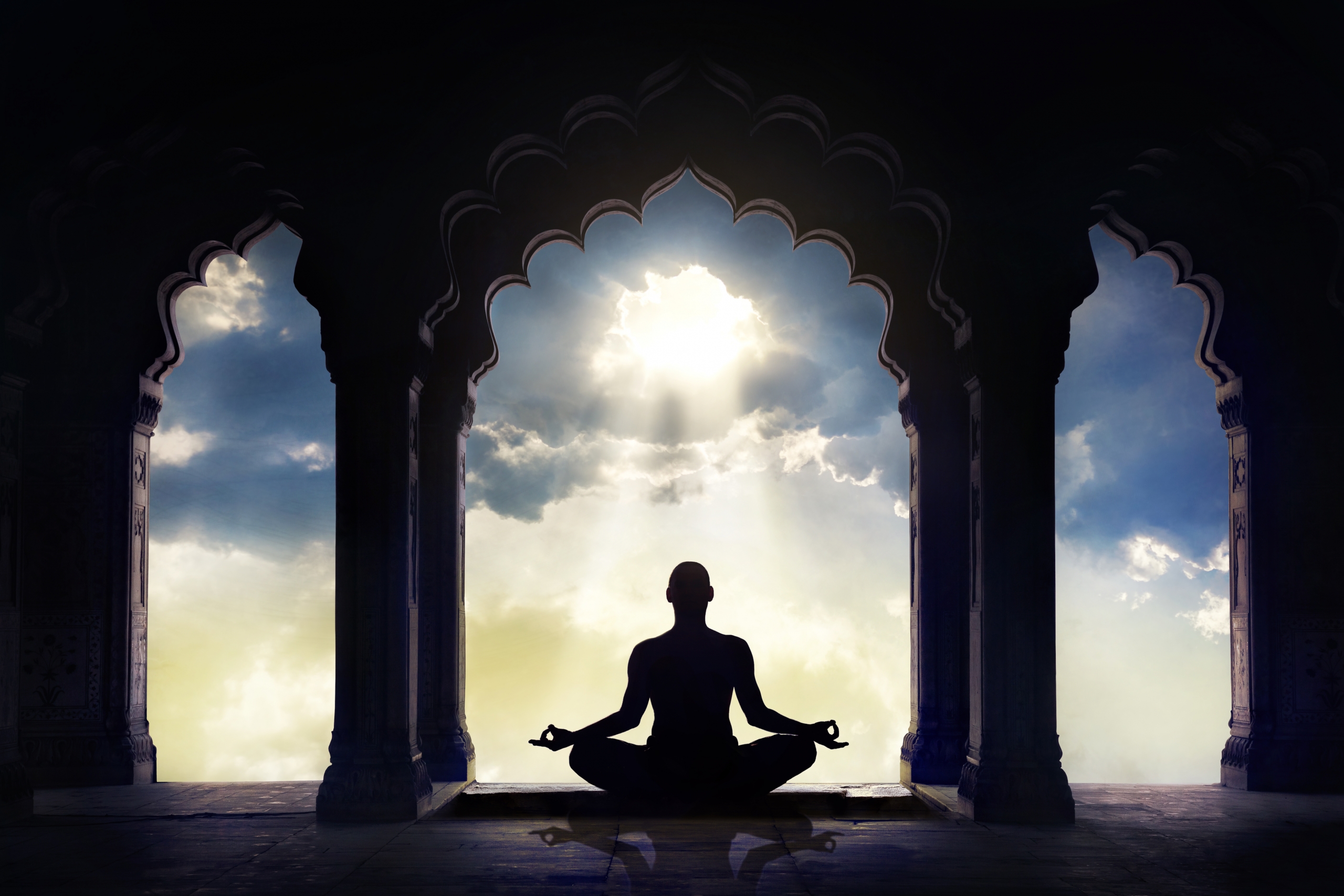Meditating in old temple with decorative arches at dramatic sunset sky with light hole in the clouds