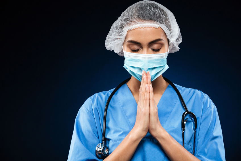 Doctor in uniform and with stethoscope making praying gesture isolated over black