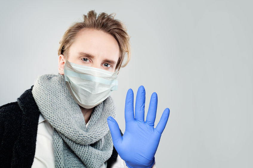 Young man in face mask and blue vinyl glove showing stop gesture