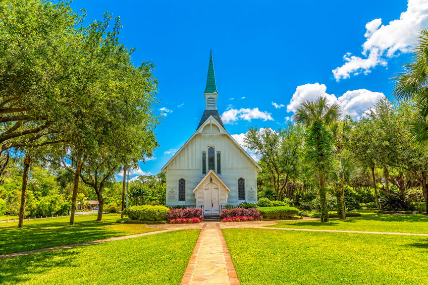 A small white church down a brick walk under blue skies