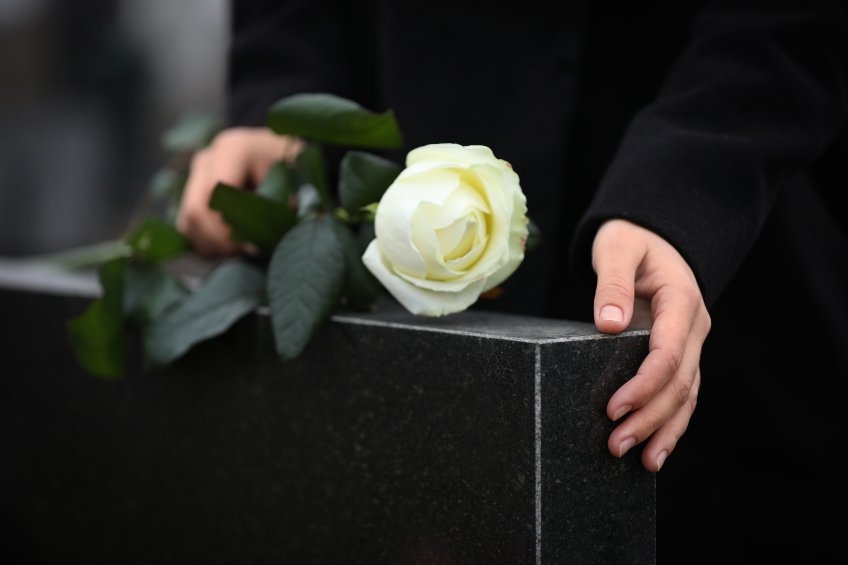 Hands holding white rose on granite tombstone