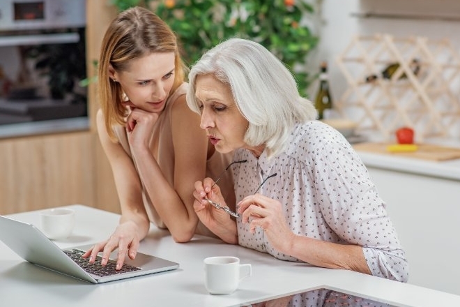 Mother and adult daughter are looking at laptop screen together to learn to use the music app